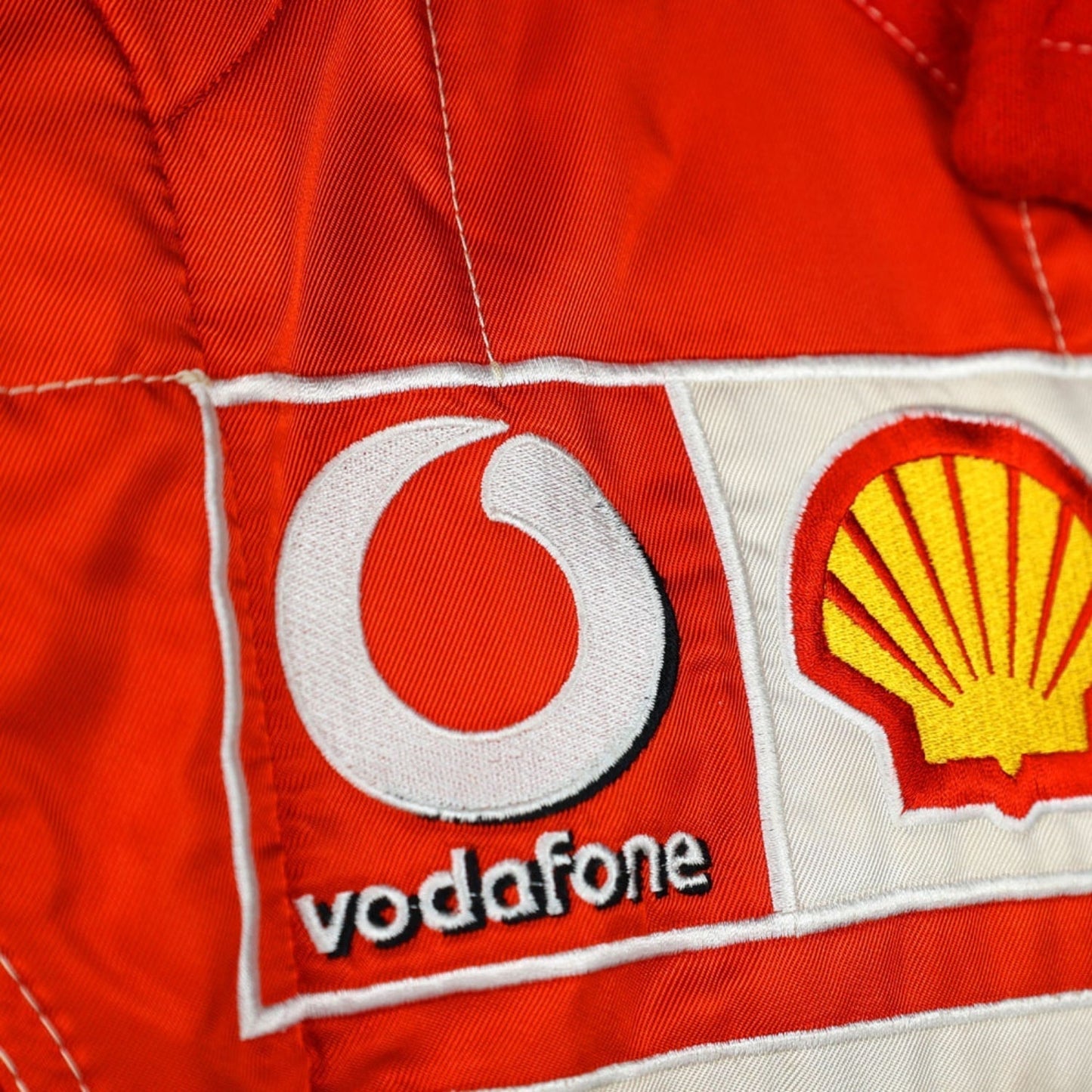 Close-up shot of Schumacher’s 2006 race suit, highlighting the detailed stitching, premium red material, and signature white branding elements.